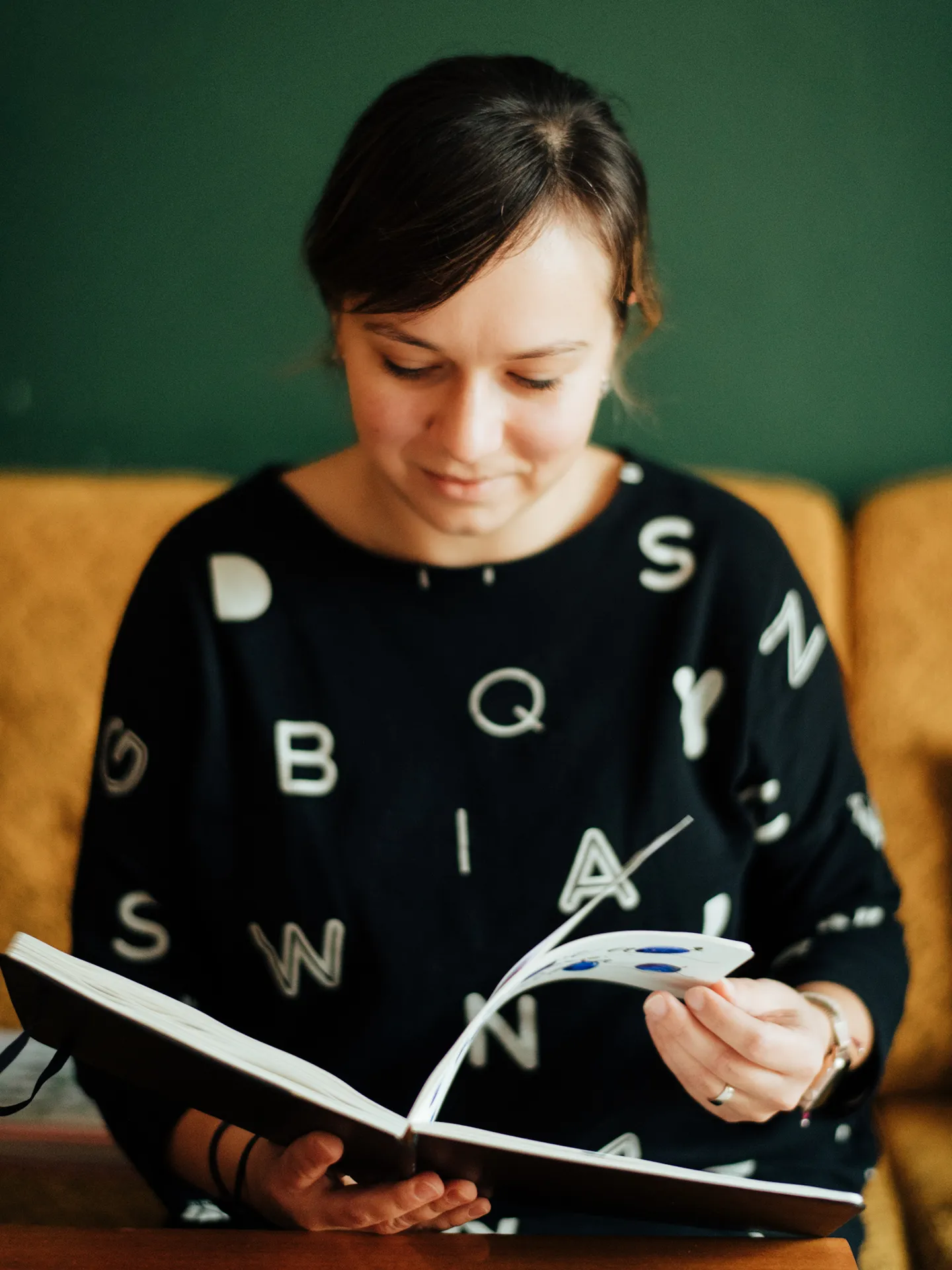 Kamila sedí v interiéri a prezerá si skicár