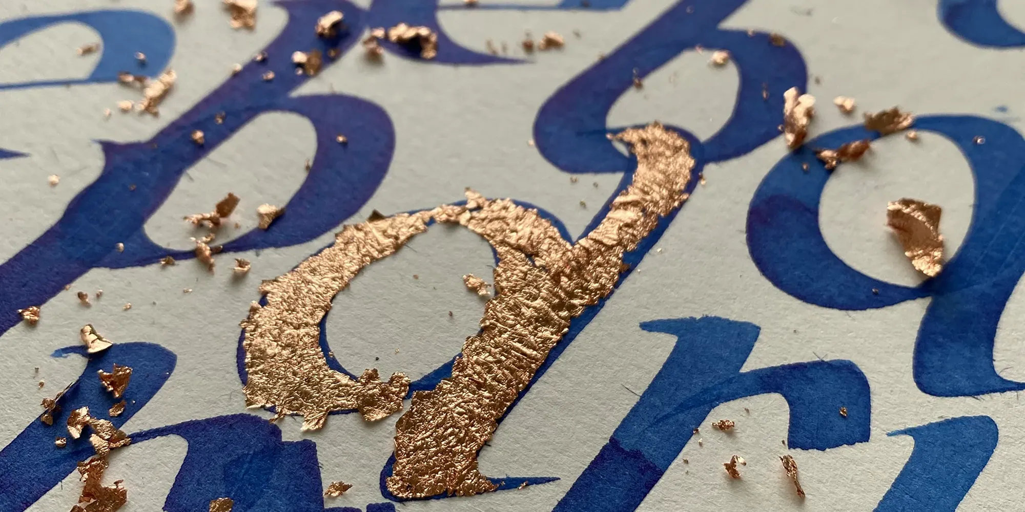 Detail kaligrafie modrým písmom s medenými zlátenými prvkami