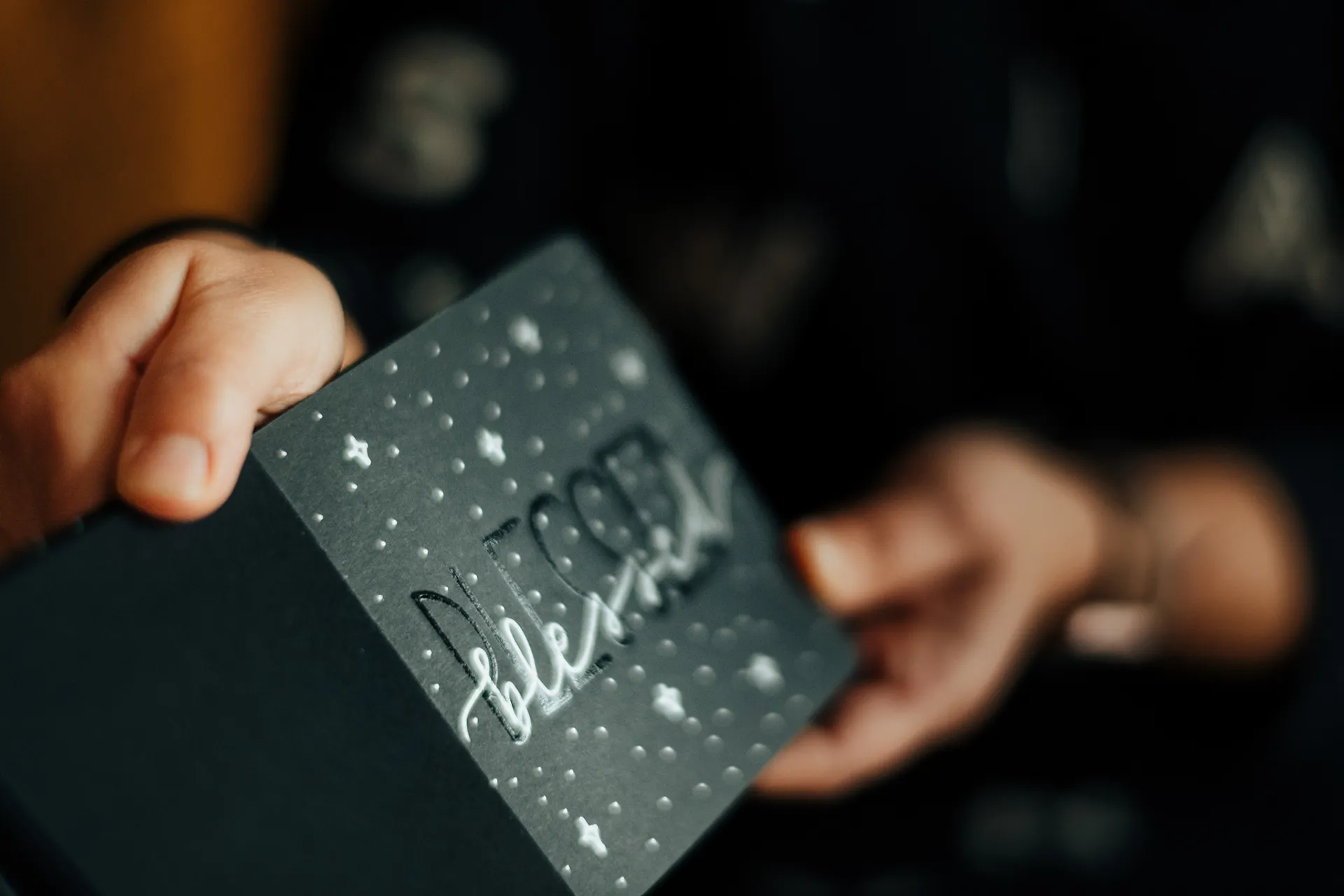 Ruka držiaca malú kartičku s bielym ručným nápisom na tmavom podklade