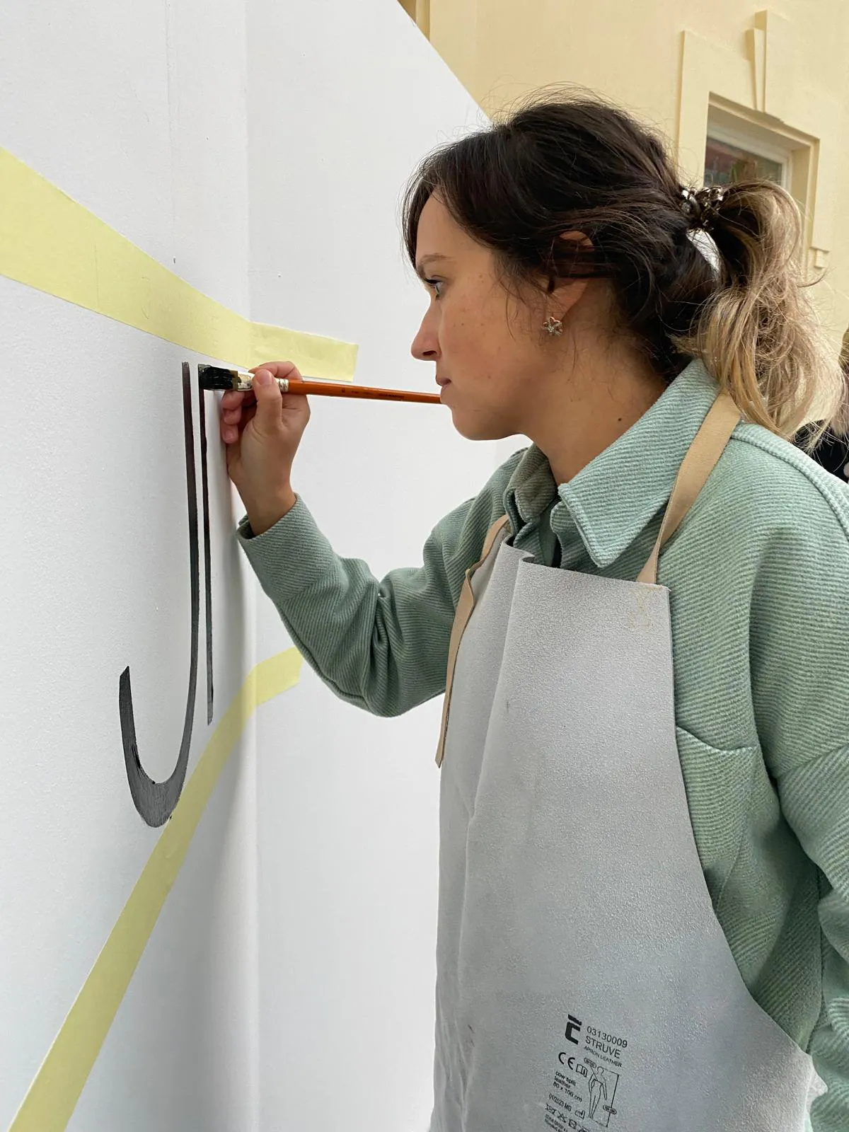 Kamila maľuje veľké písmeno na stenu štetcom počas mural letteringu