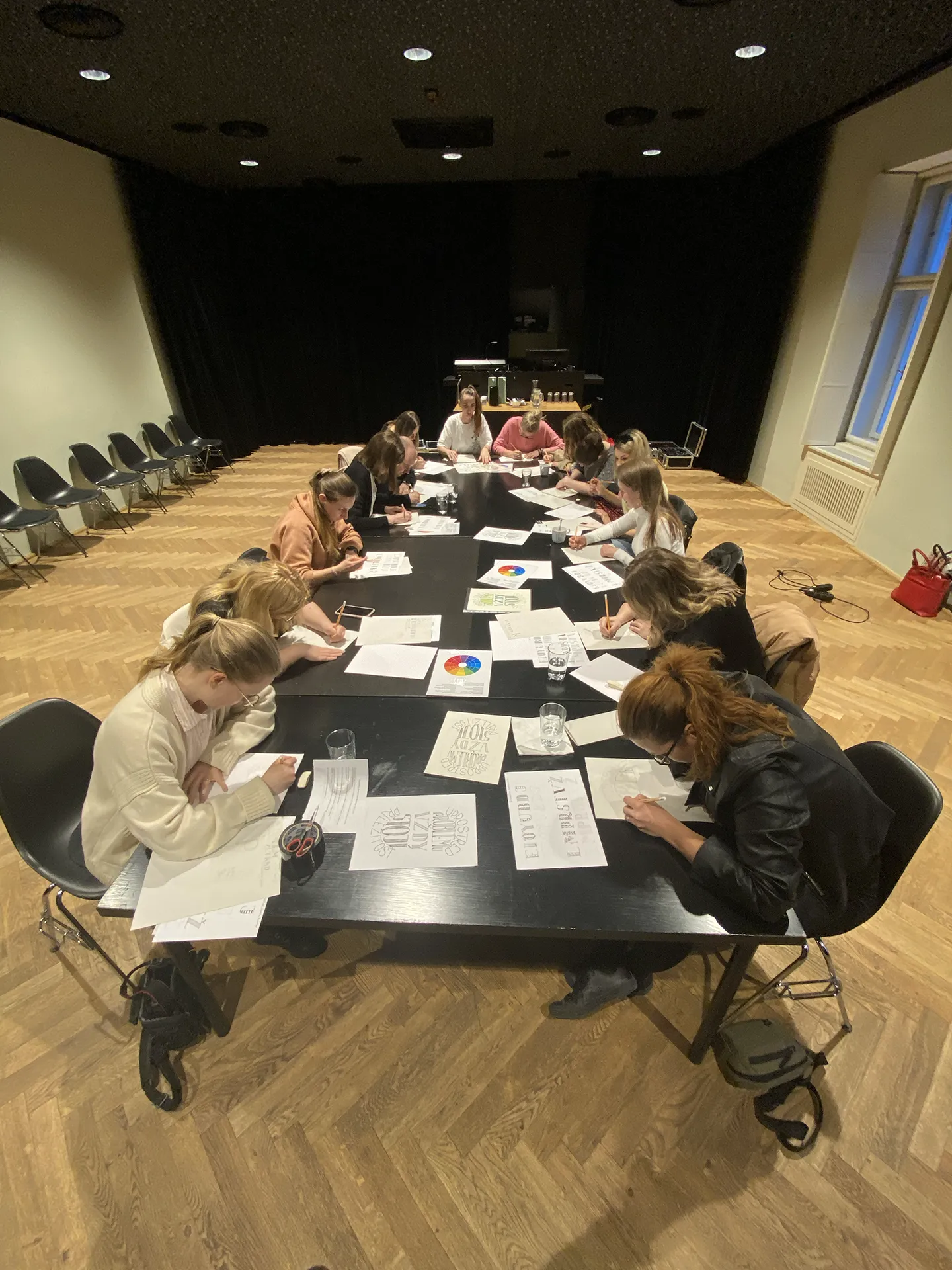 Skupinový workshop v sále, účastníci sedia okolo dlhého stola a trénujú písmo