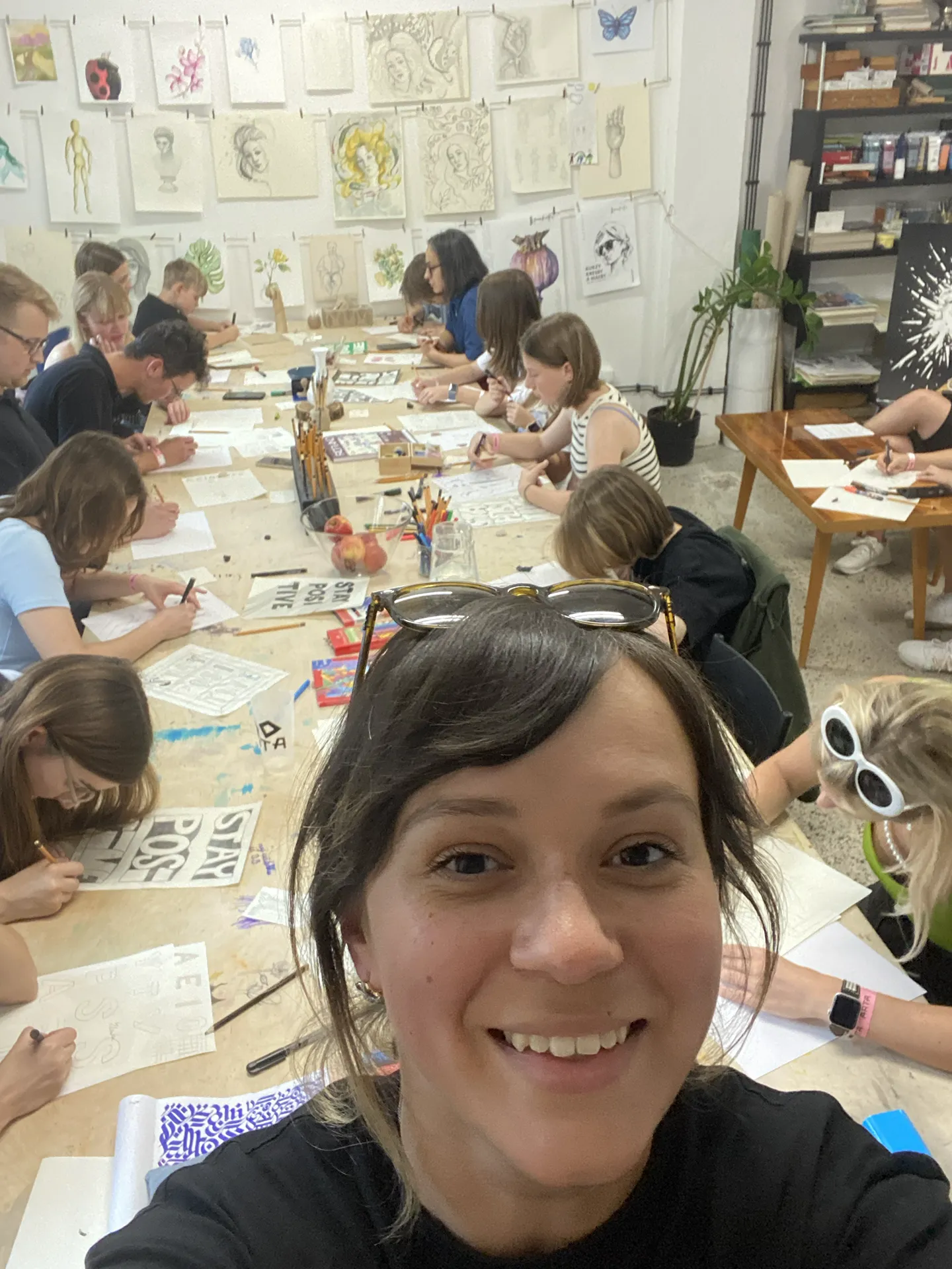 Selfie z prebiehajúceho workshopu, v pozadí ľudia píšu a na stenách visia práce