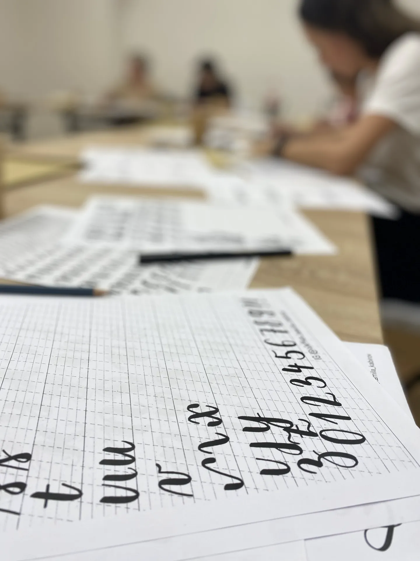 Detail stola s mriežkovanými predlohami a ukážkami ťahov písma, rozložené pracovné hárky