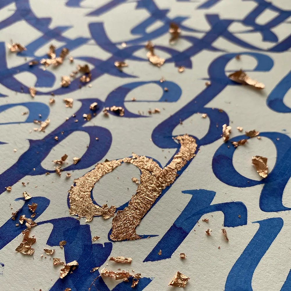 Detail modrého ručného písma s rozptýlenými kúskami medenej fólie na povrchu